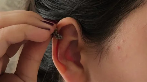 A woman hand puts a silver cuff on her ear. 動画素材 311993374