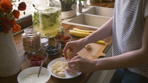 Woman hands adding fresh bananas on plate. Preparing muesli breakfast, wide shot Video stock 96241971