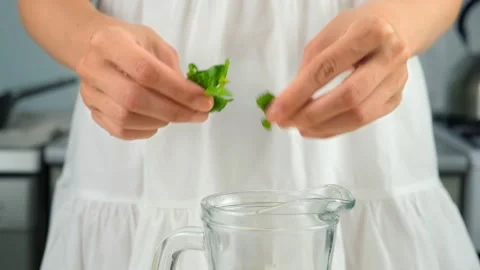 Woman hands adding mint herbs to glass jug preparing homemade lemonade. Stock Footage 313117009