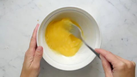 Woman hands beating eggs with fork in a white bowl on white table. Egg culinary  Stock Footage 119301067