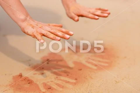 Woman hands creating shapes with red sand on the beach in aboriginal art styl Stock Photos