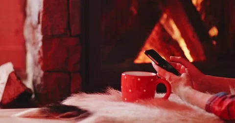 Woman Hands with Cup Using SmartPhone by the Burning Fireplace. 4K SLOW MOTION Stock-Footage 69260894