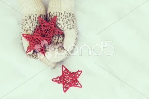 Woman Hands In Light Teal Knitted Mittens Are Holding Red Stars On Snow Backg