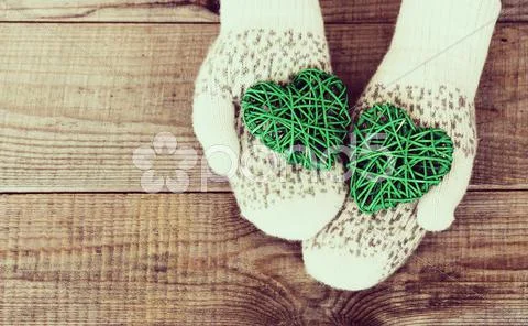 Woman Hands In Light Teal Knitted Mittens Are Holding Green Hearts On Wooden