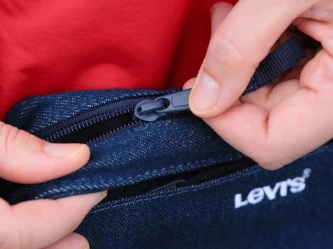 Woman hands pulling up the zip to open her Levi's denim bag. Stock Photos