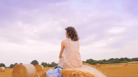 Woman with hands raised sitting on haystack and looking away. Stock Footage 100901499