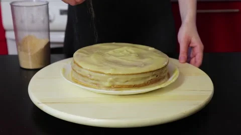 Woman hands sprinkle cake with crushed cakes and twist it on a round wooden 動画素材 130672553