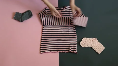 Woman hands stack kid clothes on two colored grey pink background Stock Footage 157693568