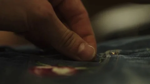 Woman hands stitch up cloth patch with rose image to denim jeans pocket Stock Footage 76539764