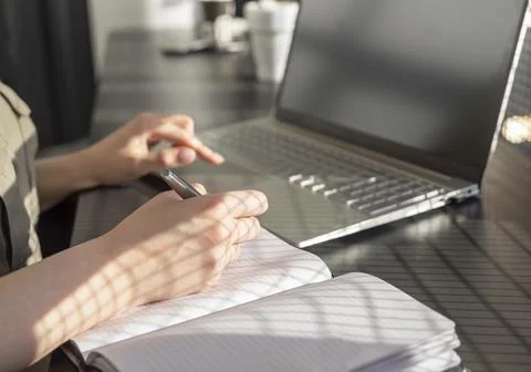 Woman hands taking notes in planner and working on laptop in cafe. Online Stock Photos