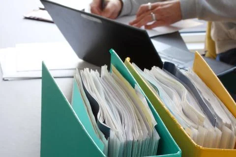 Woman hands typing on laptop computer with binders filled with papers Stock Photos