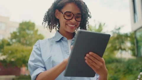 A woman happily smiling while using her tablet in a beautiful park setting Stock Footage 313267425