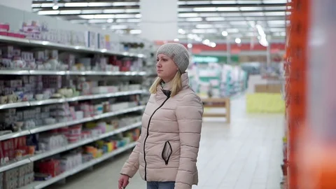 A woman in a hat and a down jacket walks through the supermarket. She looks at Video stock 102006815