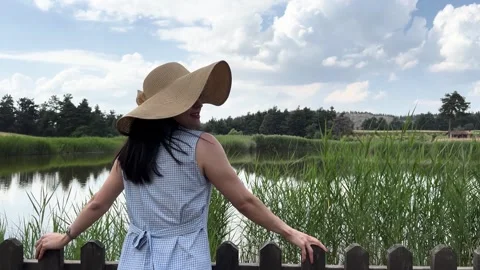 A woman with a hat by the lake smiling, back view , slow motion Stock Footage 249421453