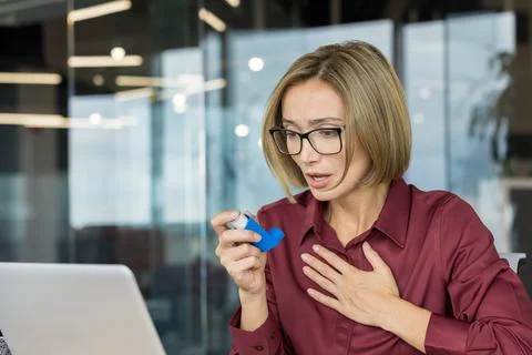 Woman having asthma attack using inhaler in office 库存照片