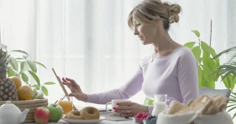 Woman having breakfast and using her tablet Stock Footage 297761048
