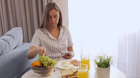 A woman is having breakfast while checking messages on her phone. Breakfast Stock Footage 278316860