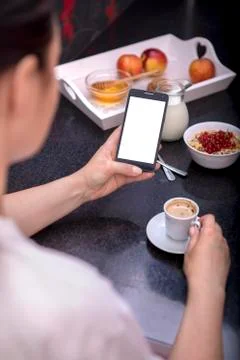 Woman having breakfast while using smartphone Фото