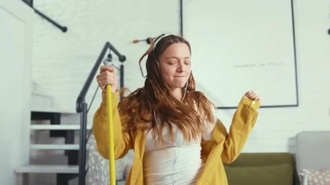 Woman having fun during clean-up singing and dancing with mop enjoying music in Stock Footage 132533360