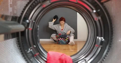 Woman having fun while doing laundry at home throwing clothes into washing ma Stock Footage 152855525