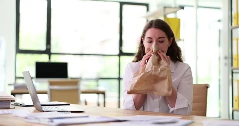 Woman having panic attack at workplace breathing into a paper bag Stock Footage 246759061