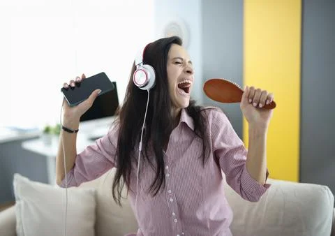 Woman with headphones and comb in her hands sings emotionally Stock Photos