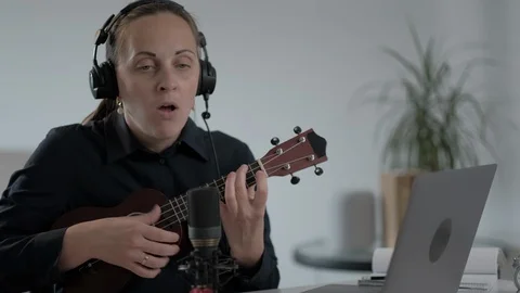 Woman in headphones using computer to learn to play her guitar or ukulele Stock Footage 128515328