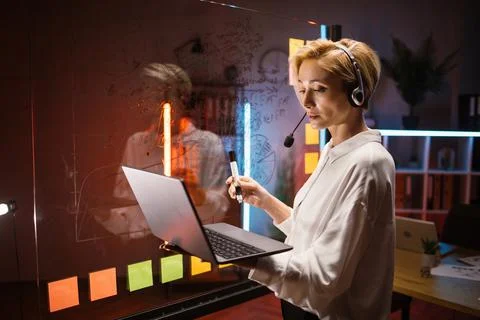Woman in headset using laptop for checking working progress, working with kanban 스톡 사진