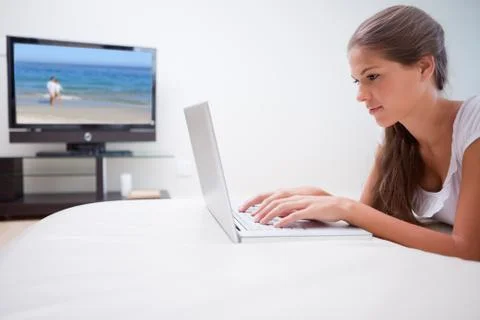 Woman on her laptop with television in the background Stock Photos