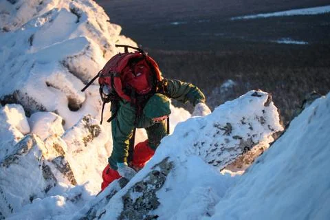 Woman hiker with backpack going thru rocks and snow on the mountain peak at cold Stock Photos