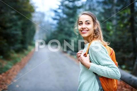 Woman hiker with small backpack, standing on the road in the forest Stock Photos