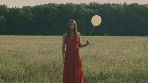 Woman holding and releasing balloon on field and forest (graded) Stock Footage