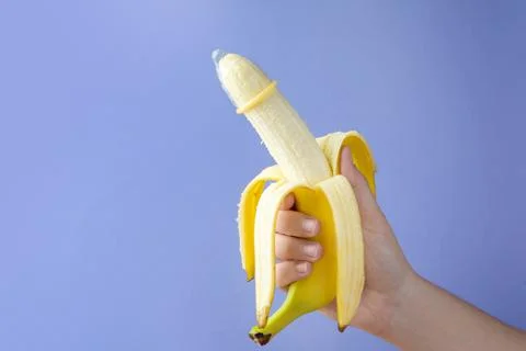 Woman holding banana in condom on light blue background, closeup and space fo Stock Photos