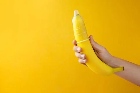 Woman holding banana in condom on orange background, closeup and space for .. Stock Photos