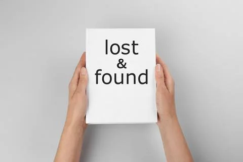 Woman holding book with phrase Lost and Found on light grey background, close Stock Photos