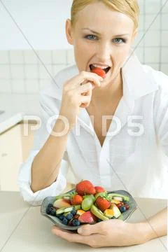 Woman Holding Bowl Of Fruit Salad, Eating Strawberry, Looking At Camera
