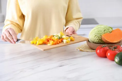 Woman holding cutting board with mix of fresh vegetables in kitchen, closeup Stock Photos