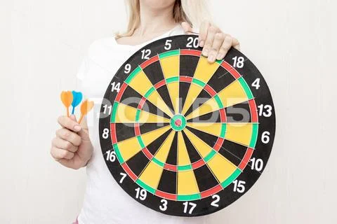 Woman holding a dart board and darts in hands close up, aiming and targetting Stock Photos