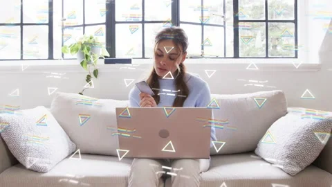 Woman holding device on sofa, switching to laptop, typing for tech work, Stock Footage 333774595