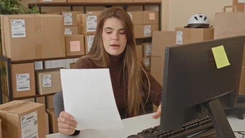 Woman holding a document and checking parcel labels at a computer desk amid.. Stock Footage 347807092