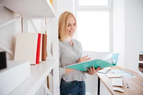 Woman holding folder with documents while standing at book shelf Stockfoto's