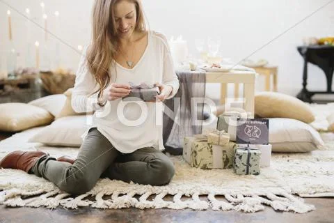 A woman holding a gift wrapped parcel, sitting on the floor. Stock Photos