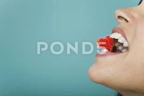 Woman holding heart-shaped candy between teeth, cropped Stock-Fotos