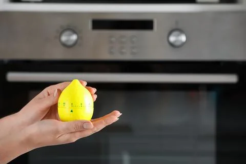 Woman holding kitchen timer in shape of lemon near oven, closeup. Space for t Stock Photos