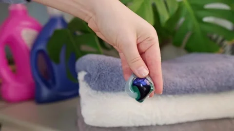 Woman holding a laundry capsule, with a stack of freshly washed towels in the ba Stock Footage 295285959
