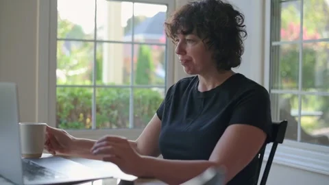 Woman holding mug while working on laptop at home Stock Footage 319920803
