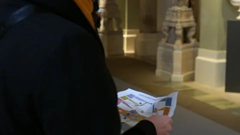 Woman holding a museum map while walking through a sculpture gallery lined with 库存影片 332518008
