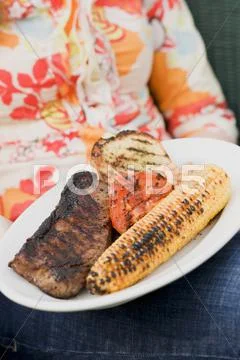 Woman holding a plate of grilled steak and accompaniments Stock Photos