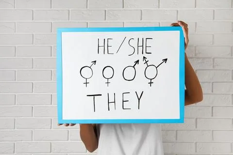 Woman holding sign with gender pronouns and symbols near white brick wall Stock Photos