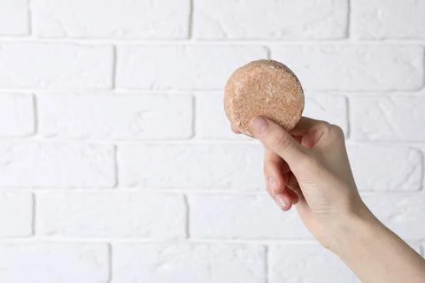 Woman holding solid shampoo bar against brick white wall, closeup. Space for  스톡 사진